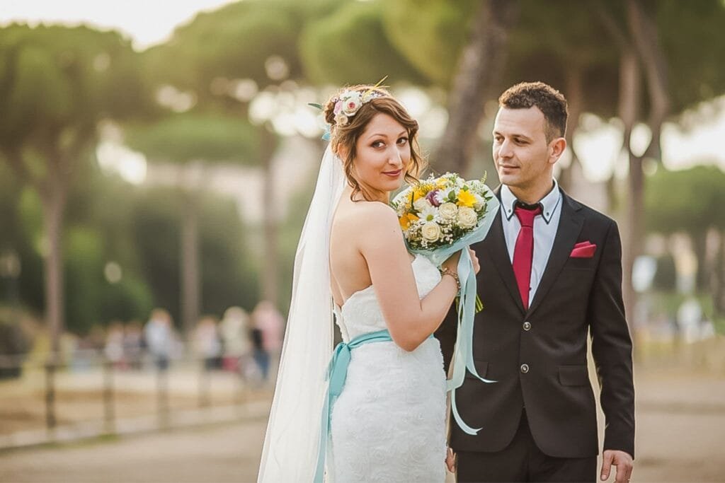 Mireasă cu buchet pastel și mire elegant în parc roman, fotografie de nuntă naturală