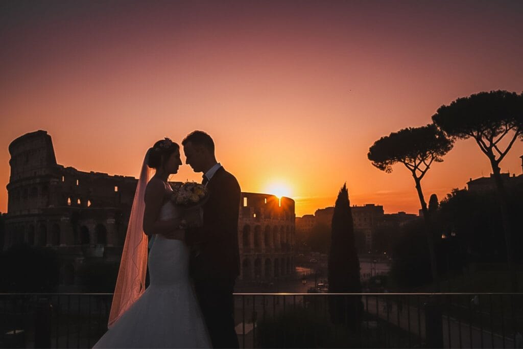 Silhouette romantica degli sposi Irina e Gio al tramonto davanti al Colosseo di Roma